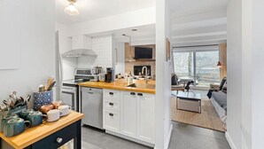 Una cucina moderna con mobili bianchi, un piano di lavoro in legno e un piano cottura integrato. C'è un'area pranzo con un divano e un tavolino.