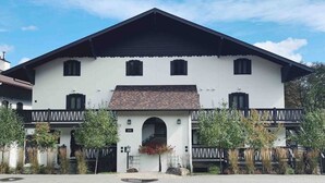 Un edificio de dos pisos con fachada blanca, techo negro y un balcón con barandilla negra.