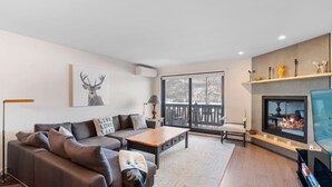 A modern living room with a sofa, coffee table, and fireplace. - Spacious Condo with Lake and Mountain View (Mont-Tremblant)