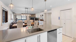 A modern kitchen with a central island, stainless steel appliances, pendant lighting, and a view to the dining area. - Spacious Condo with Lake and Mountain View (Mont-Tremblant)