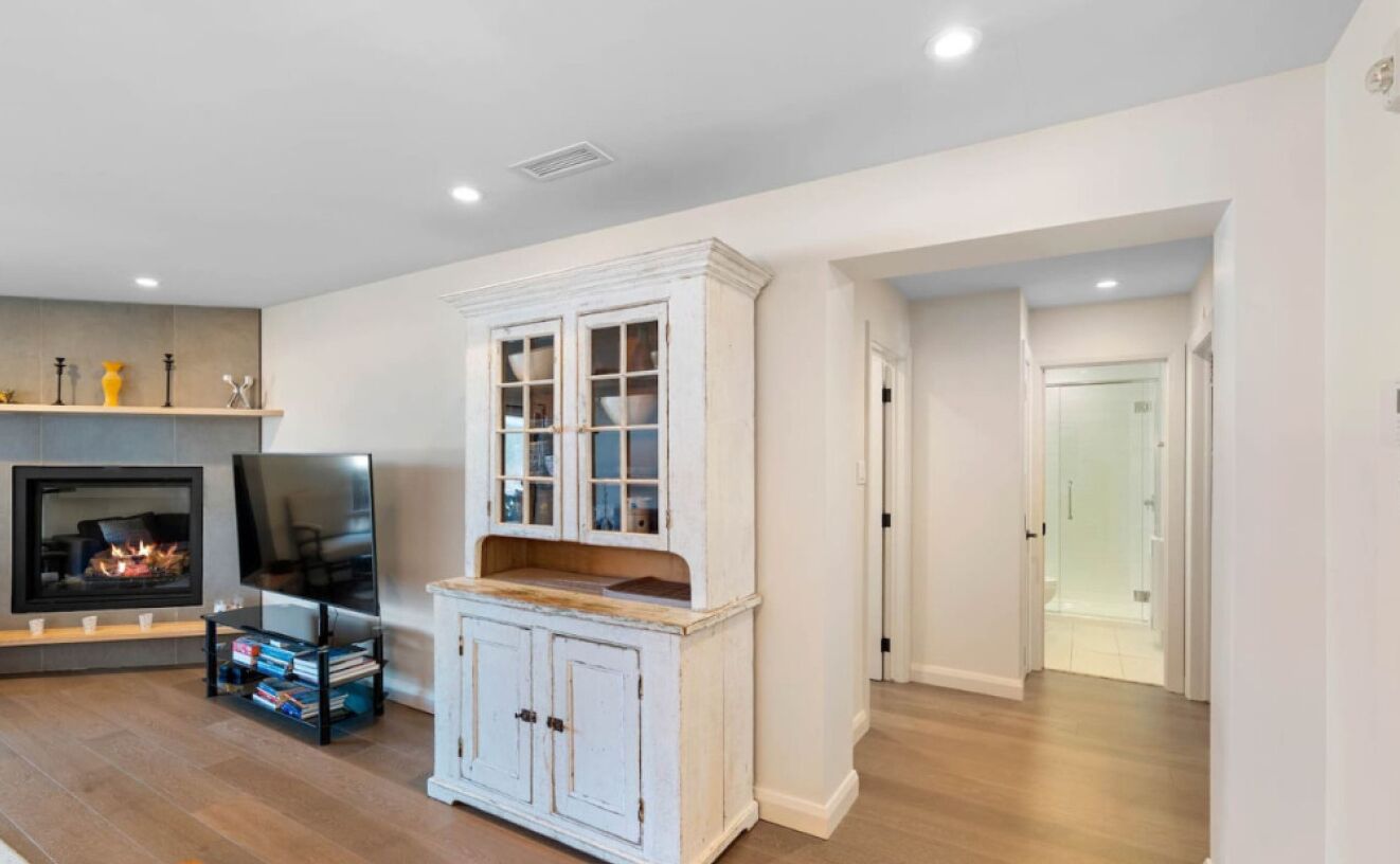 A living room with a fireplace, a television, and a white cabinet with glass doors.