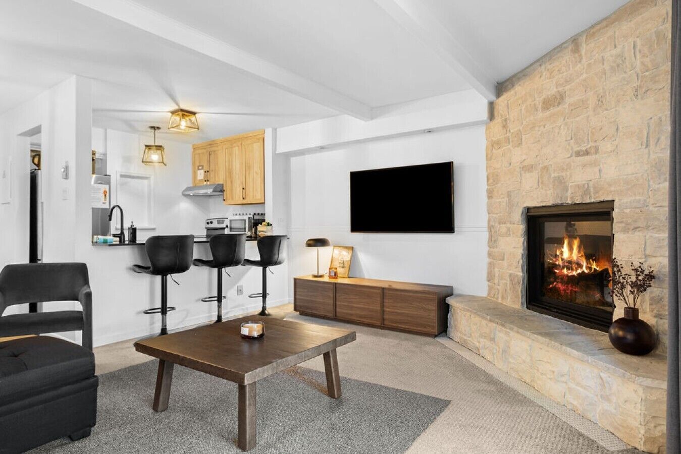 A modern living room with a fireplace, a flat-screen TV, and a kitchen area with wooden cabinets and a gas stove.