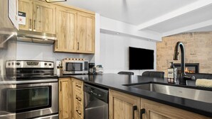 Una cocina moderna con electrodomésticos de acero inoxidable, armarios de madera, encimera negra y chimenea.