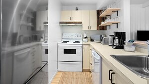 A modern kitchen with white cabinetry, a built-in oven, a microwave, a coffee maker, and a wooden shelf above the counter.