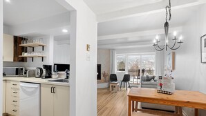A modern kitchen with white cabinets, a dining area with a wooden table, and a chandelier.