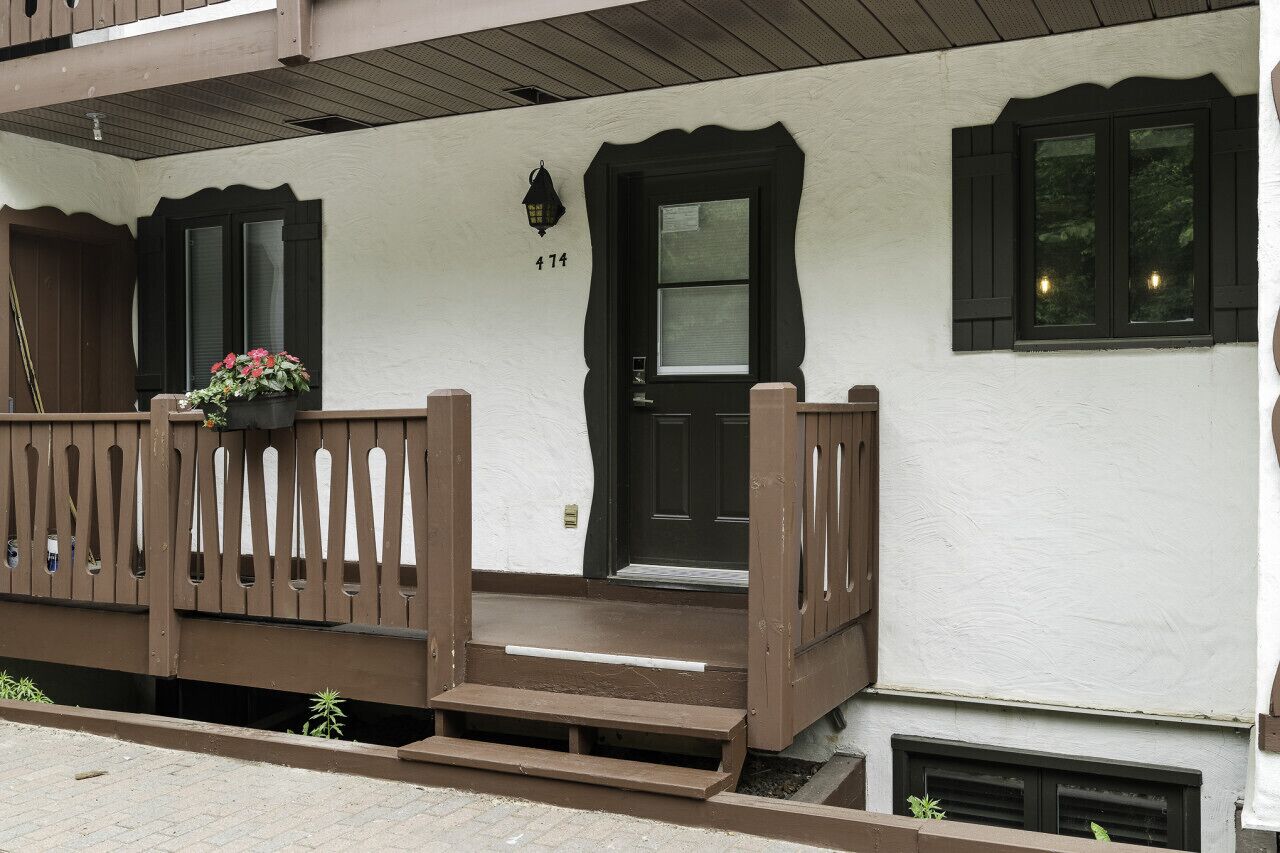 A building with a white exterior, black shutters, and a brown wooden balcony with steps leading to a door marked with the number 47.