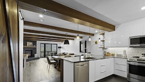 Una cucina moderna con mobili bianchi, un'isola centrale, elettrodomestici in acciaio inossidabile e un'area pranzo con camino.