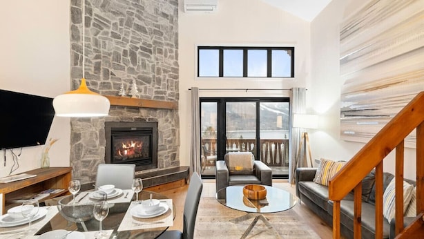 A modern living room with a stone fireplace, a dining area with a glass table, and a cozy seating area with a sofa and armchairs.