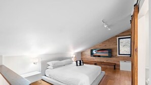 A modern bedroom with a sloped ceiling, a bed with white bedding, a mounted TV, and a wooden wall panel.