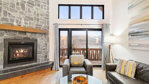 A cozy living room with a stone fireplace, a glass coffee table, and a leather sofa.