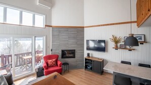 En moderne stue med en rød lænestol, et fjernsyn ophængt på væggen og et spiseområde med et bord og stole.