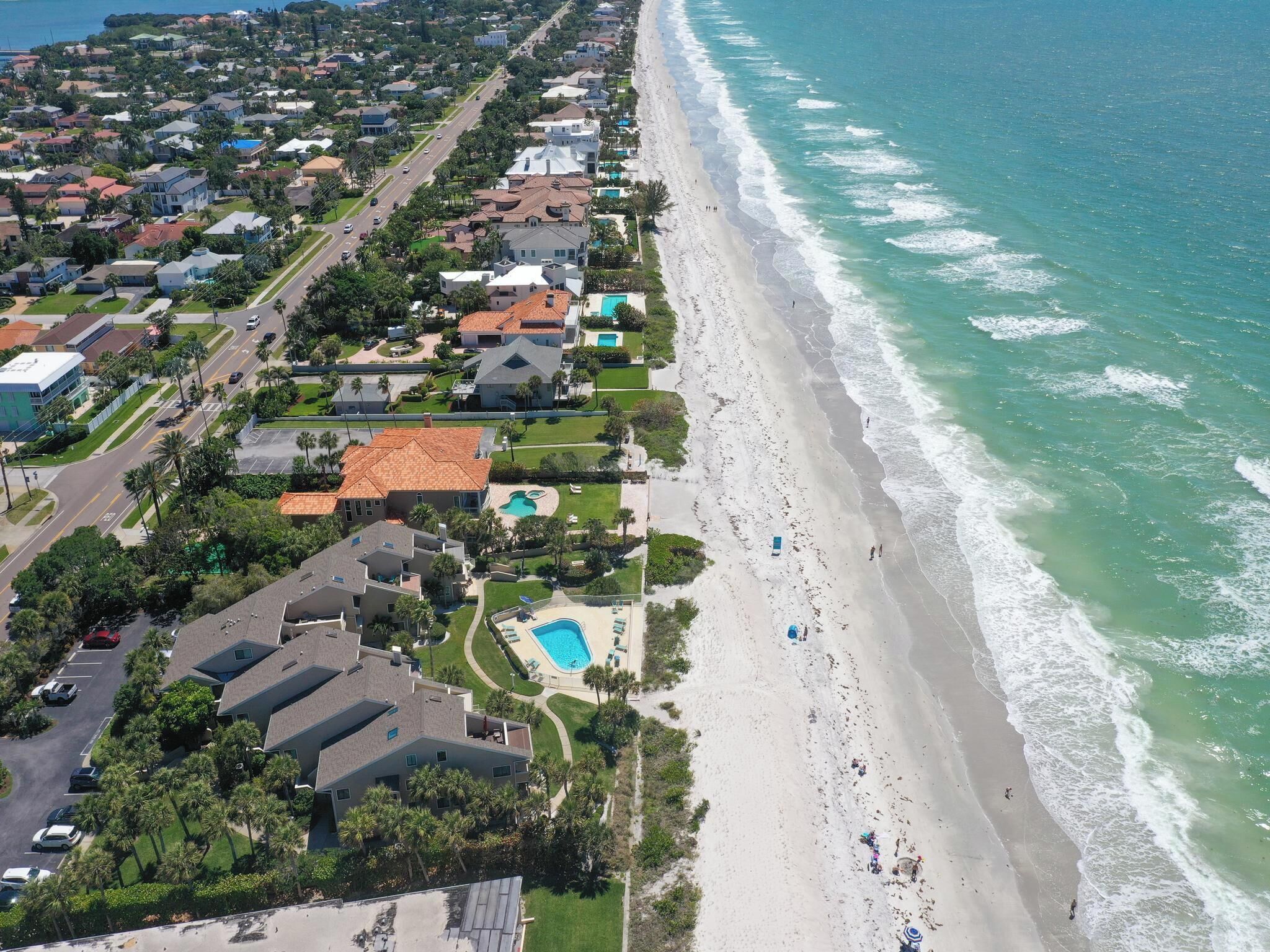 Vista aérea de una zona residencial costera con casas, una playa y una piscina.