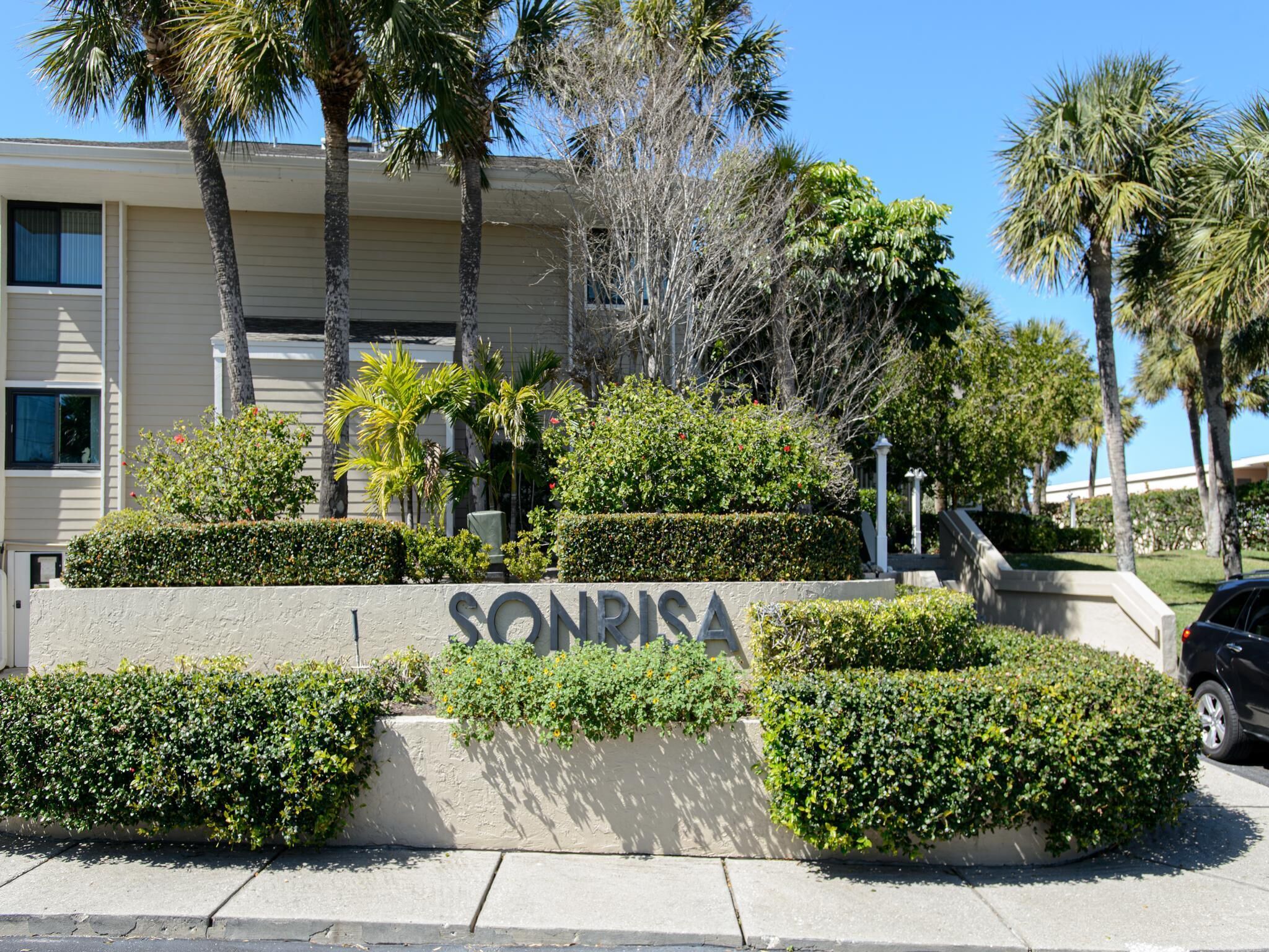 Un bâtiment portant l’enseigne « SONRISA », entouré d’un aménagement paysager soigné et de palmiers.