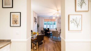 A hallway with framed artwork, a dining area with a table and chairs, and a window with blinds. - Luxury Living with Stunning Views (Southampton)