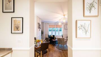A hallway with framed artwork, a dining area with a table and chairs, and a window with blinds.