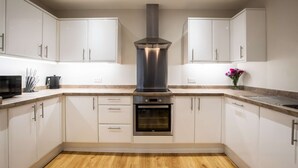 A modern kitchen with white cabinets, a stainless steel range hood, an oven, and a microwave. - Luxury Living with Stunning Views (Southampton)