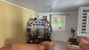 A living room with a sofa, ottoman, and a wooden entertainment unit. - Villa à la Campagne (Sainte -Luce)