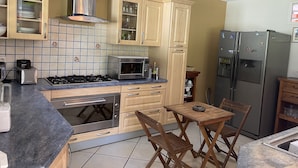 A kitchen with wooden cabinets, a gas stove, a microwave, a refrigerator, and a wooden table with chairs. - Villa à la Campagne (Sainte -Luce)