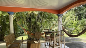 A covered outdoor seating area with wooden furniture, a hammock, and a view of lush greenery. - Villa à la Campagne (Sainte -Luce)