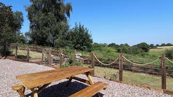 Une table de pique-nique installée dans un cadre naturel, avec une clôture en corde et des arbres en arrière-plan.