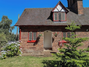 Une maison à deux étages, construite en briques, avec un toit à deux versants, une porte d’entrée et un petit porche.