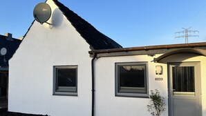 Ein weißes Gebäude mit Satellitenschüssel, zwei Fenstern, einer Tür und einem Blumentopf.