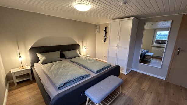 Ein Schlafzimmer mit Bett, Nachttischen, einer Bank, einem Kleiderschrank und einem Fenster mit Blick.