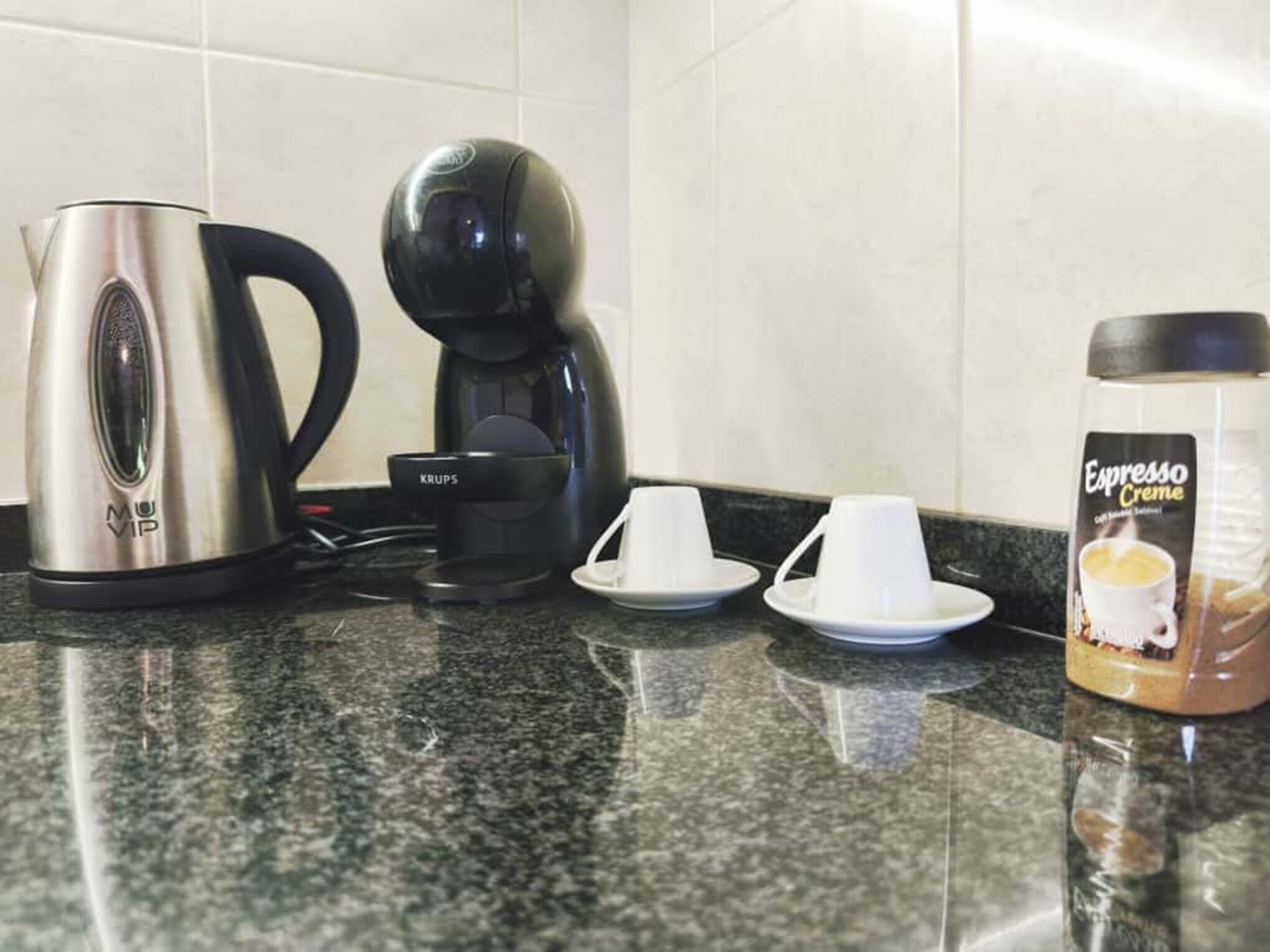 Keittiön työtasolla on kahvinkeitin, Krupsin kahvipannu, kaksi valkoista kuppia ja purkki espressoon tarkoitettua kermaa.