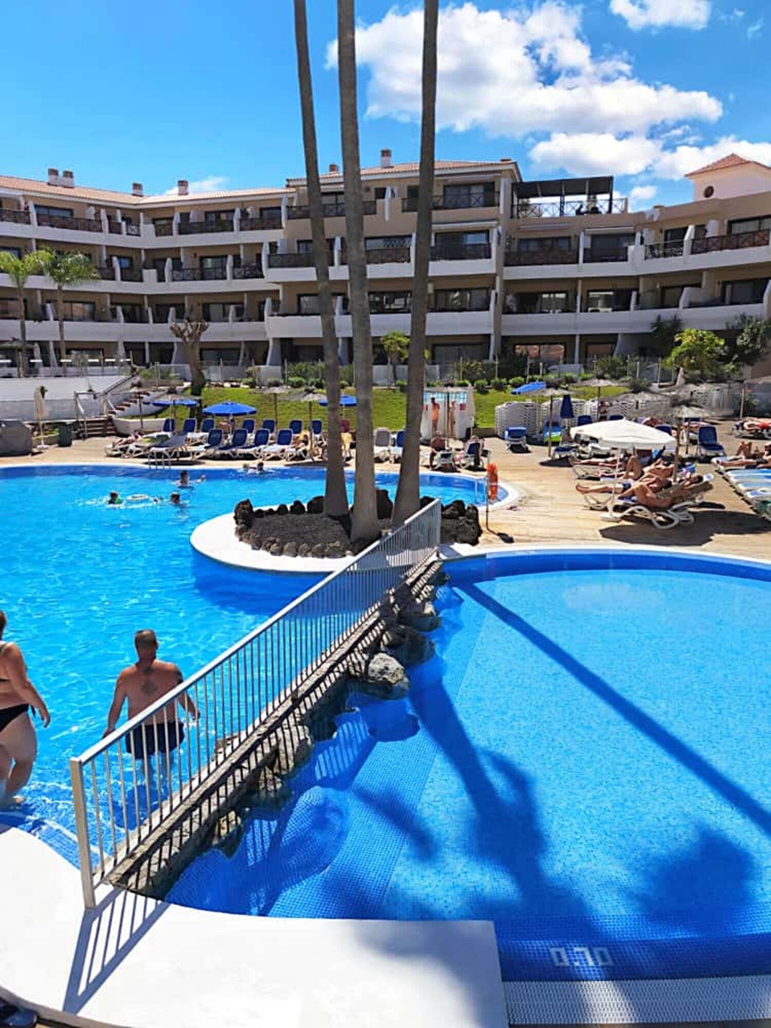 Un espace piscine d’hôtel doté de plusieurs niveaux de balcons, de chaises longues et d’une piscine à l’eau d’un bleu cristallin.