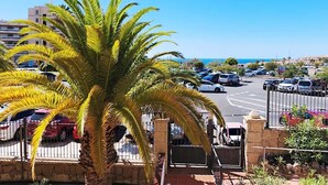A parking area with cars, a palm tree, and a view of the sea. - Bib's Pool Side Apartment & Ocean View (CN)