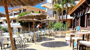 An outdoor patio area with stone flooring, thatched umbrellas, and outdoor seating. - Bib's Pool Side Apartment & Ocean View (CN)