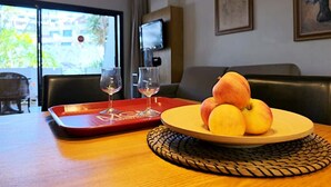A dining area with a table set for two, featuring a fruit bowl and two wine glasses on a red tray. - Bib's Pool Side Apartment & Ocean View (CN)