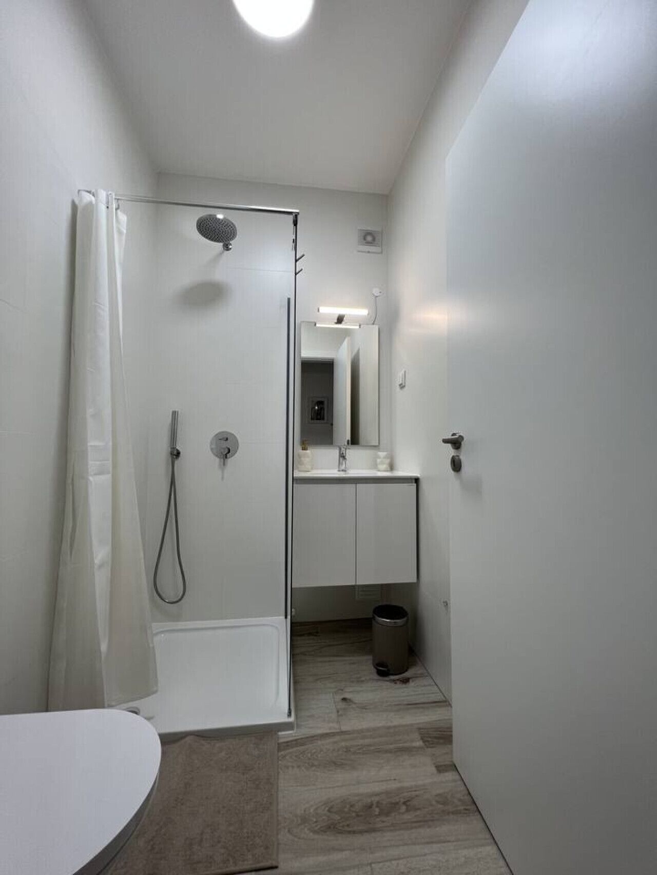 Ein schmales Badezimmer mit Dusche, Toilette und Waschbecken.