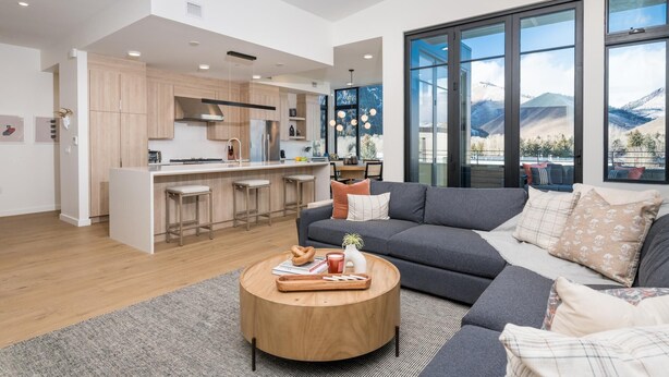 A modern living room with a large sofa, a coffee table, and a view of the mountains through large windows. - 5 Min to Bald Mountain | Sawtooth Views (Ketchum)