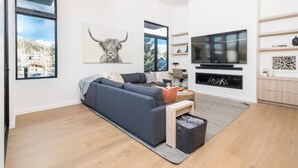A modern living room with a grey sofa, a coffee table, a TV mounted on the wall, and a fireplace. - 5 Min to Bald Mountain | Sawtooth Views (Ketchum)