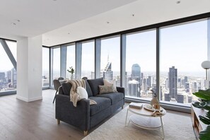A modern living room with a large window, a grey sofa, a small round table, and a city view.