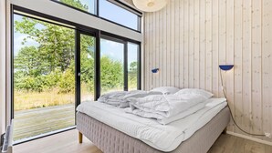 A bedroom with a bed, a view of greenery through large windows, and a wooden wall. - 3 bedroom pet friendly home in Glesborg (Glesborg)