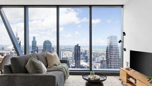 A modern living room with a large window, a sofa, a coffee table, and a TV. - A 2BR Apt with Amazing City Views, FREE Parking (Melbourne)