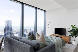 A modern living room with a large window, a sofa, a TV, and a plant.
