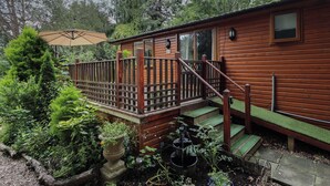 A wooden cabin with a wooden deck, surrounded by lush greenery and a garden. - Kantankye Lodge (Skegness)
