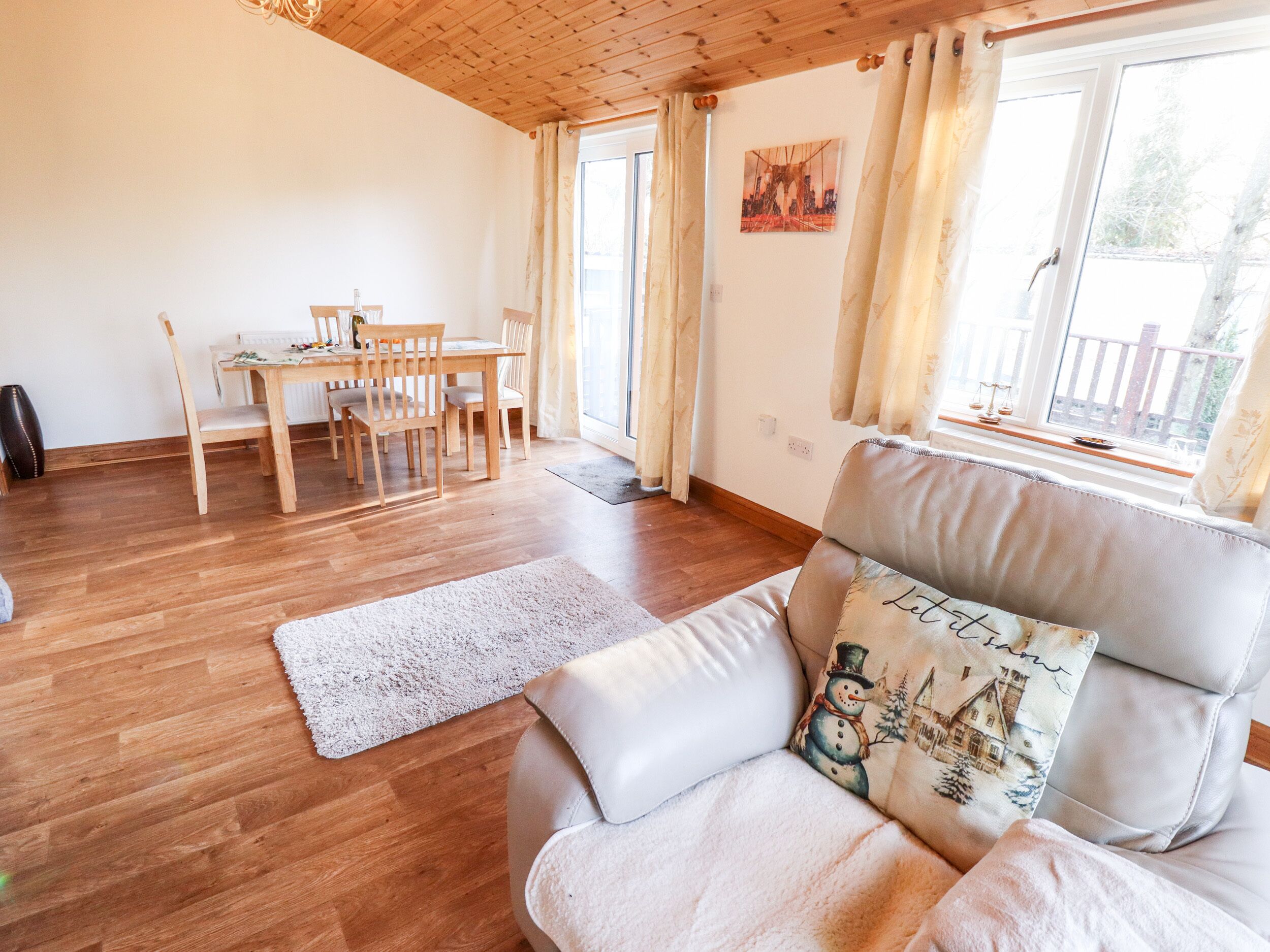 Un salon chaleureux avec un plafond en bois, un coin repas avec une table et des chaises, et une grande fenêtre agrémentée de rideaux.