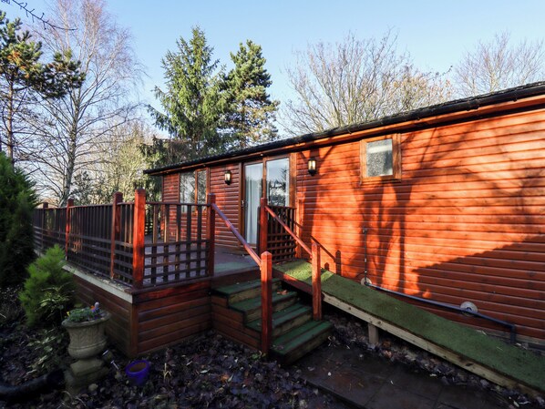 A wooden cabin with a deck, a door, and a window. - Kantankye Lodge (Skegness)