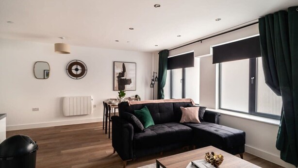 Ein modernes Wohnzimmer mit einer schwarzen Couch, einem Holztisch und einem Essbereich im Hintergrund.