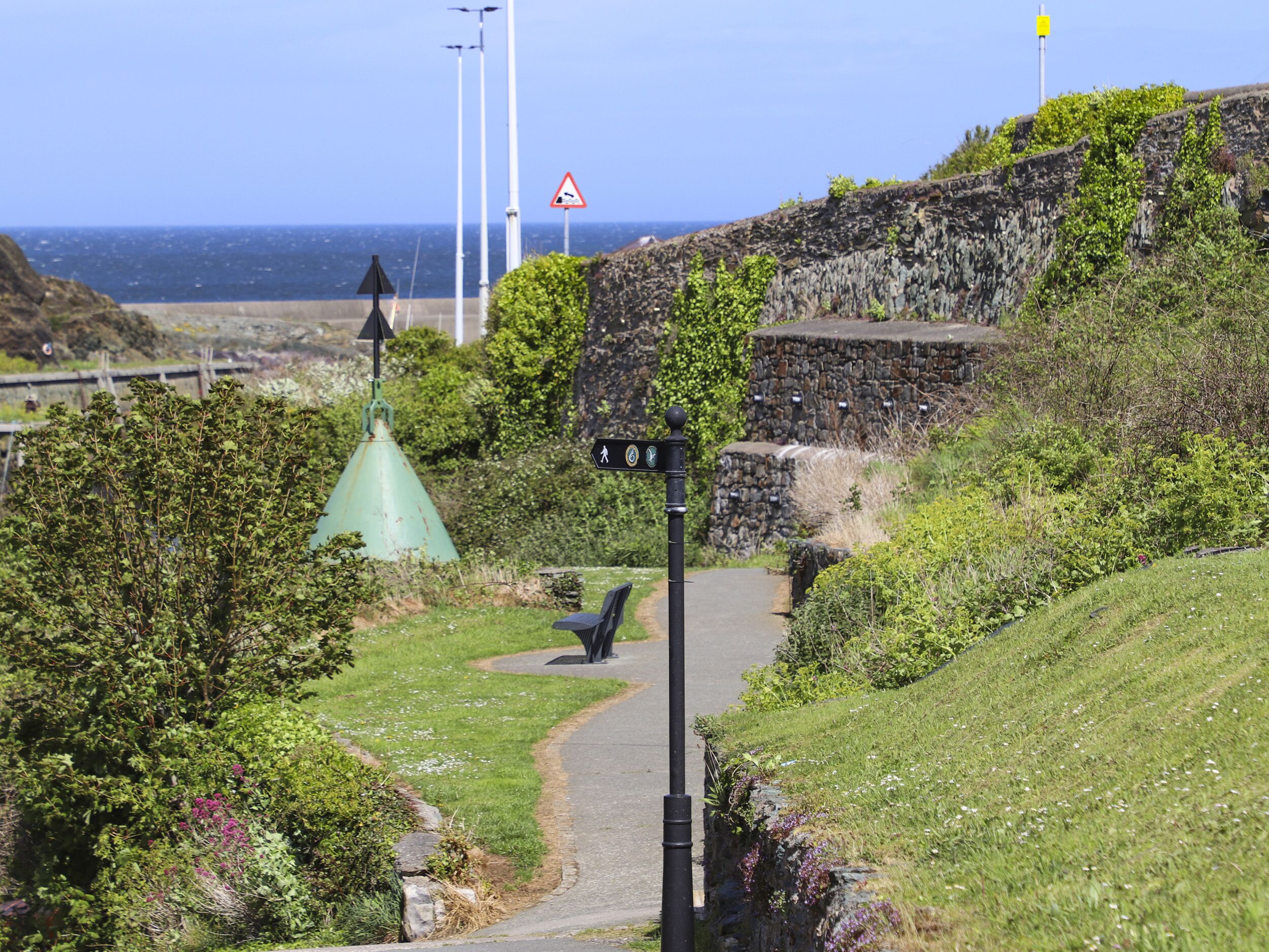 A pathway leading to a coastal area with a stone wall and a green structure.