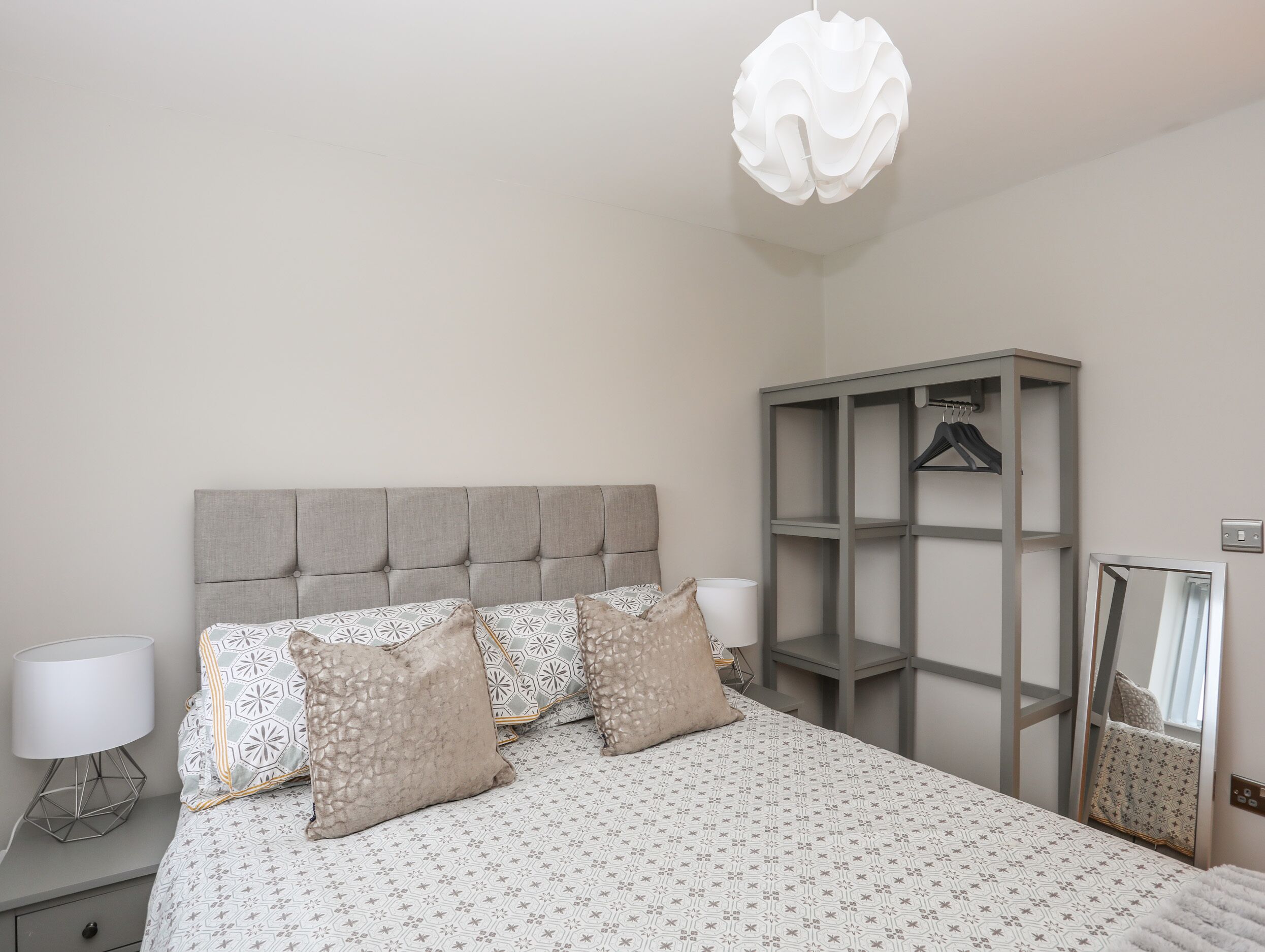 A neatly arranged bedroom with a bed, a bedside lamp, a wardrobe, and a hanging light fixture.