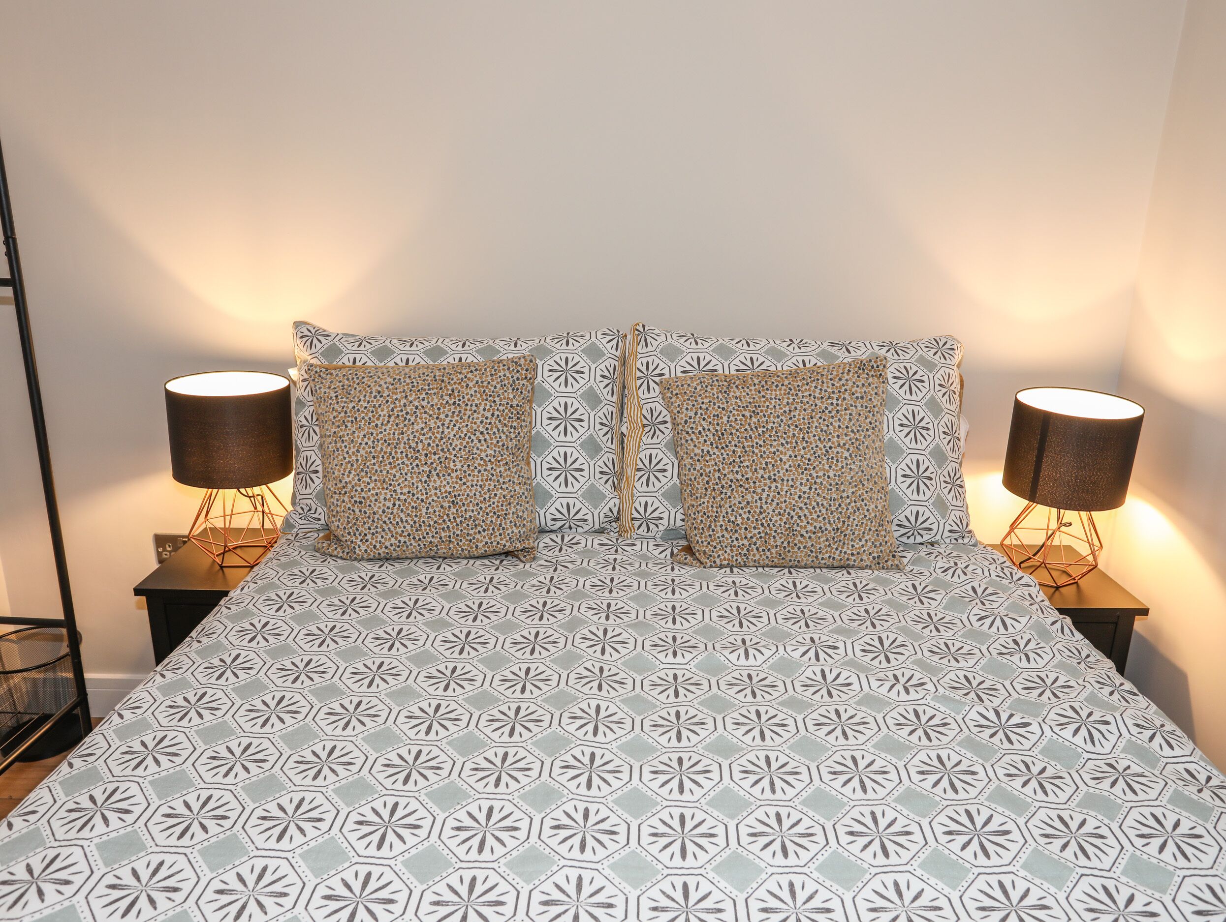 Een bed met een gebedruid sprei, twee vierkante kussens en twee bedlampjes op nachtkastjes.