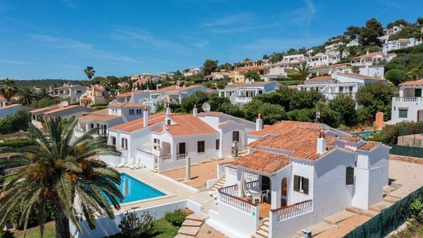 Un quartier résidentiel avec des maisons blanches, une piscine et un paysage vallonné en arrière-plan.