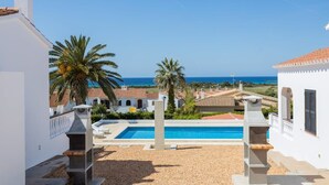 Un espace piscine offrant une vue dégagée sur la mer, entouré de bâtiments blancs et de palmiers.