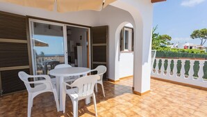 Une terrasse avec une table et des chaises blanches, une porte vitrée donnant sur l’intérieur et une vue sur la mer.