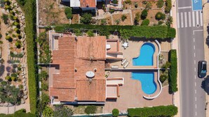 Vista aérea de una propiedad con piscina, un patio cubierto y una carretera adyacente.